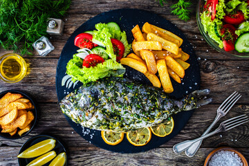 Grilled sea bream, French fries and fresh vegetables on wooden table