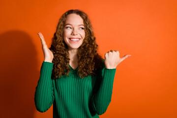 Photo of impressed funky lady dressed green shirt looking showing thumb emtpy space isolated orange...