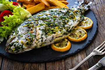 Grilled sea bream, French fries and fresh vegetables on wooden table