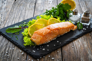 Smoked salmon with lemon and greens on black stony plate on wooden background
