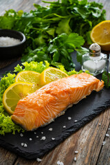 Smoked salmon with lemon and greens on black stony plate on wooden background
