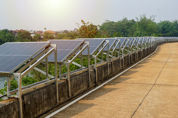 row of solar panels is installed on a concrete barrier along the river to generate solar electricity for water pumps for use in agriculture. - obrazy, fototapety, plakaty