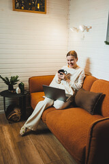 Smiling woman sitting on sofa at home and talking on phone, working on laptop online, freelancer modern lifestyle. - obrazy, fototapety, plakaty