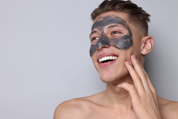 Handsome man with clay mask on his face against light grey background. Space for text
