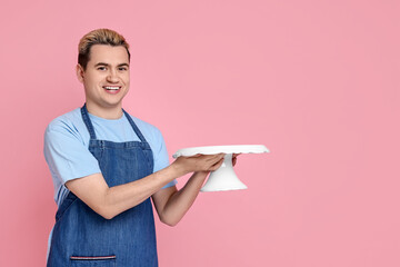 Portrait of happy confectioner holding cake stand on pink background, space for text