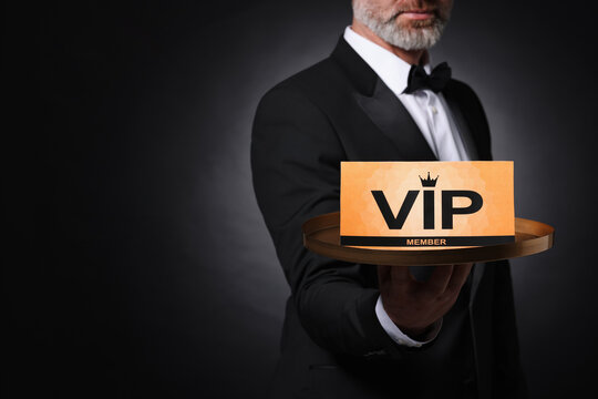 Man holding tray with VIP sign on black background, closeup. Space for text