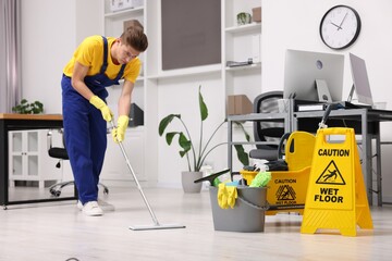 Cleaning service worker washing floor with mop. Bucket with supplies and wet floor sign in office - obrazy, fototapety, plakaty