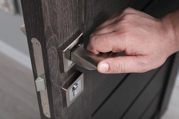 Man opening wooden door indoors, closeup of hand on handle