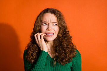Photo of scared nervous lady dressed green shirt biting fingers looking emtpy space isolated orange...