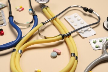 Stethoscopes and pills on beige background, closeup. Medical tools