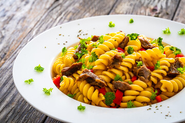 Pasta with roasted pork meat - noodles witch pork cheeks and vegetables on wooden background
