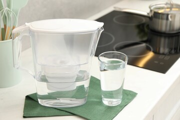 Water filter jug and glass on white countertop in kitchen