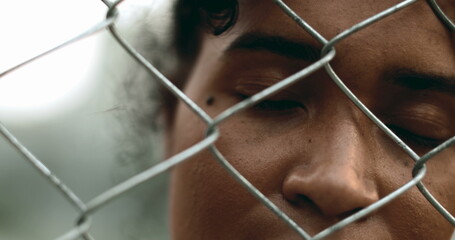 One young black woman trapped behind a fence, close-up hand and face closing eyes in solitude. 20s...