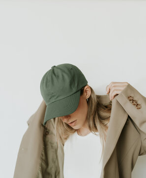 Young Stylish Woman Putting On A Beige Blazer And Wearing A Green Hat