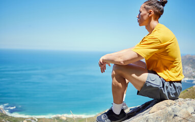 Man, hiking and rest on mountain with ocean, ideas or vision with mockup space on blue sky background. Person, relax and memory with peace on rocks by sea, thinking and nature for trekking adventure