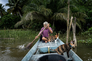 An elderly fisherman rowing a river boat with his cats in Thailand