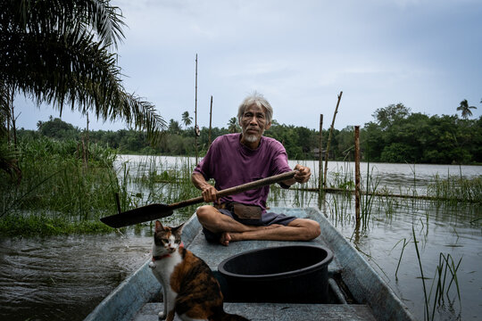Portrait of a fisherman rowing a river boat with his cat in Thailand