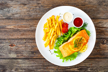 Fried salmon steak, French fries and fresh vegetable salad served on wooden table
