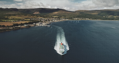 Scotland ocean, passenger ferry aerial view in coastal water of Firth-of-Clyde Gulf. Ship crossing from Brodick terminal to Scottish mainland. Cityscape at green valleys. Cinematic shot