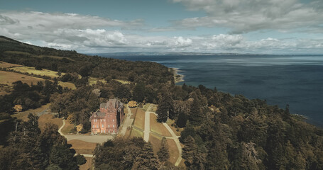Scotland landscape, medieval castle aerial view: trees and ocean shore at Brodick Bay, Arran Island. Majestic scenery of green leafy wood at coastline. Beauty of Scottish nature. Cinematic shot