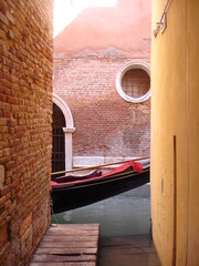 Black and red Gondola in partial view in sunlit side street with elaborate brickwork in Venice...
