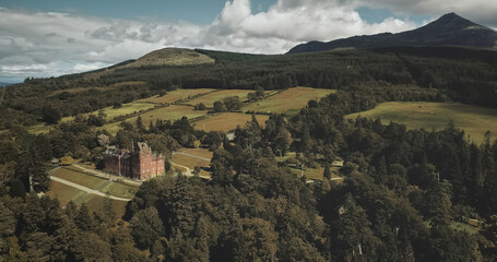 Scotland mountains, old castle aerial panning shot: designed landscapes of garden and parks near building. Beautiful woods, hills, valleys in horizon at summer day. Dramatic scenery view