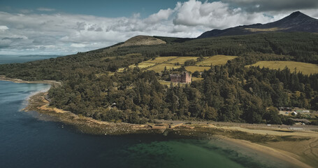 Scotland Arran island landscape aerial zooming view: forests, meadows, mountains at summer day. Clouds on skyline near Goat Fell peak. Epic scene of Atlantic coastline. Cinematic shot