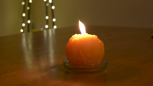 Yellow round wax candle with flickering yellow flame in a dark room