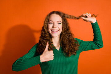 Photo of cool confident lady dressed green shirt holding hair curl showing thumb up isolated orange color background