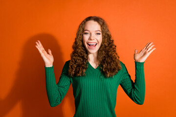 Photo of excited impressed lady dressed green shirt rising arms hands emtpy space isolated orange color background