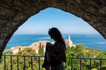 Tourist woman with baby carrier under window arch of city walls Piransko obzidje. Scenic aerial...