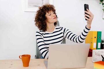 Young woman smiling while taking selfie with smartphone in office