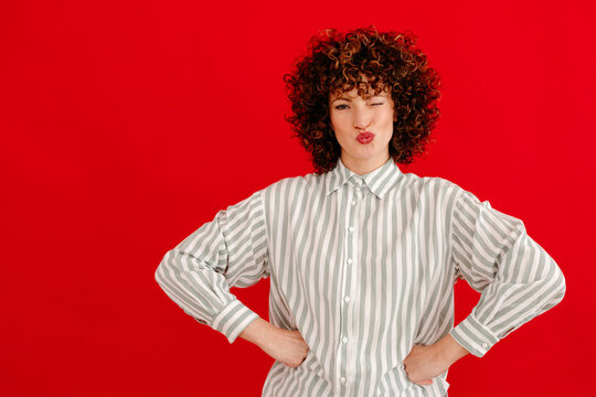 Smiling young curly haired woman making pouting lips in studio