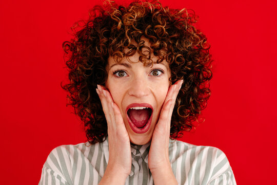 Shocked curly haired woman looking at camera in studio