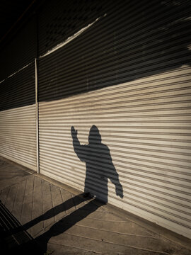 Shadow of someone wearing a puffy jacket waving against a metal door
