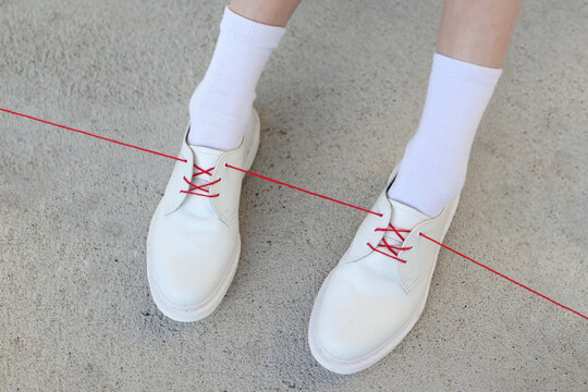 White shoes with one red lace/ribbon. Illustration of red thread 