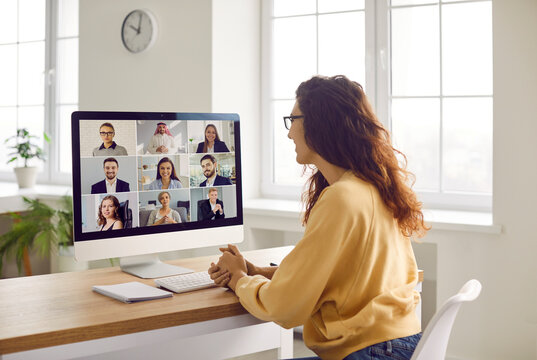 Corporate business team having a remote meeting. Young woman in casual clothes sitting at her desk at home, attending an online conference, looking at the computer screen, and smiling