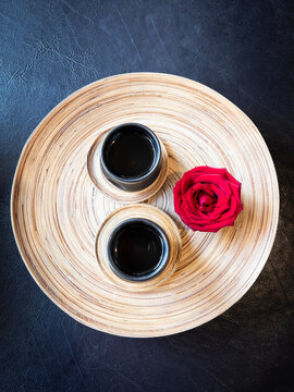 Wooden plate with two ceramic cups of hot tea next to a blooming rose
