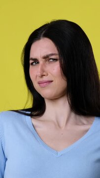 Portrait of a dissatisfied Caucasian woman reacted on smelly odor over yellow background. Displeasure and discontent. Vertical video.