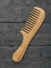 Wooden comb with a handle on a dark wooden background.