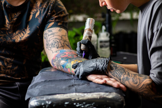 Woman tattoo artist tattooing man in salon