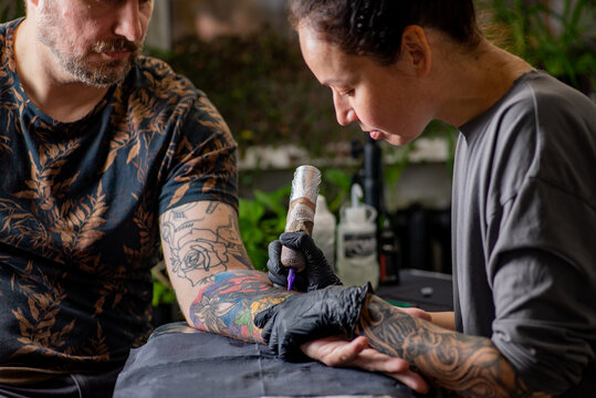 Woman tattoo artist tattooing man in salon