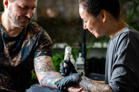 Woman tattoo artist tattooing man in salon