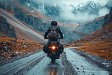 A lone motorcyclist navigates a winding mountainous road amidst the enveloping fog and stark landscape - obrazy, fototapety, plakaty