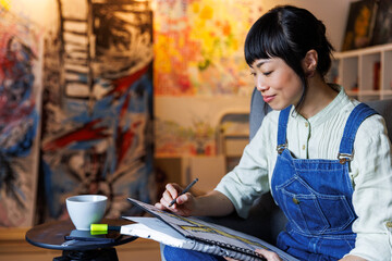 Smiling asian artist drawing on book at art studio 