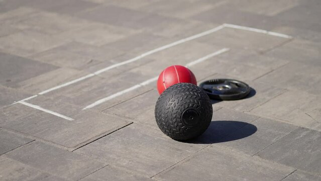 Outdoor Fitness Equipment on Pavement. Red medicine ball and black tire on paved ground, outdoor workout scene.