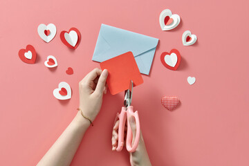 Female hands cutting red hearts while making love card