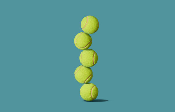 Five tennis balls stacked in tower balancing in studio