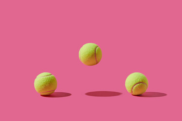 Tennis balls with levitating one over pink studio background