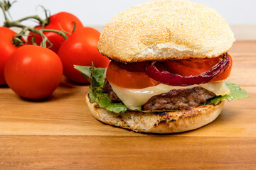 cheeseburger with Havarti cheese tomatoes and red onions and lettuce on a toasted cornmeal bun on a wooden table with bun open showing ingredients

